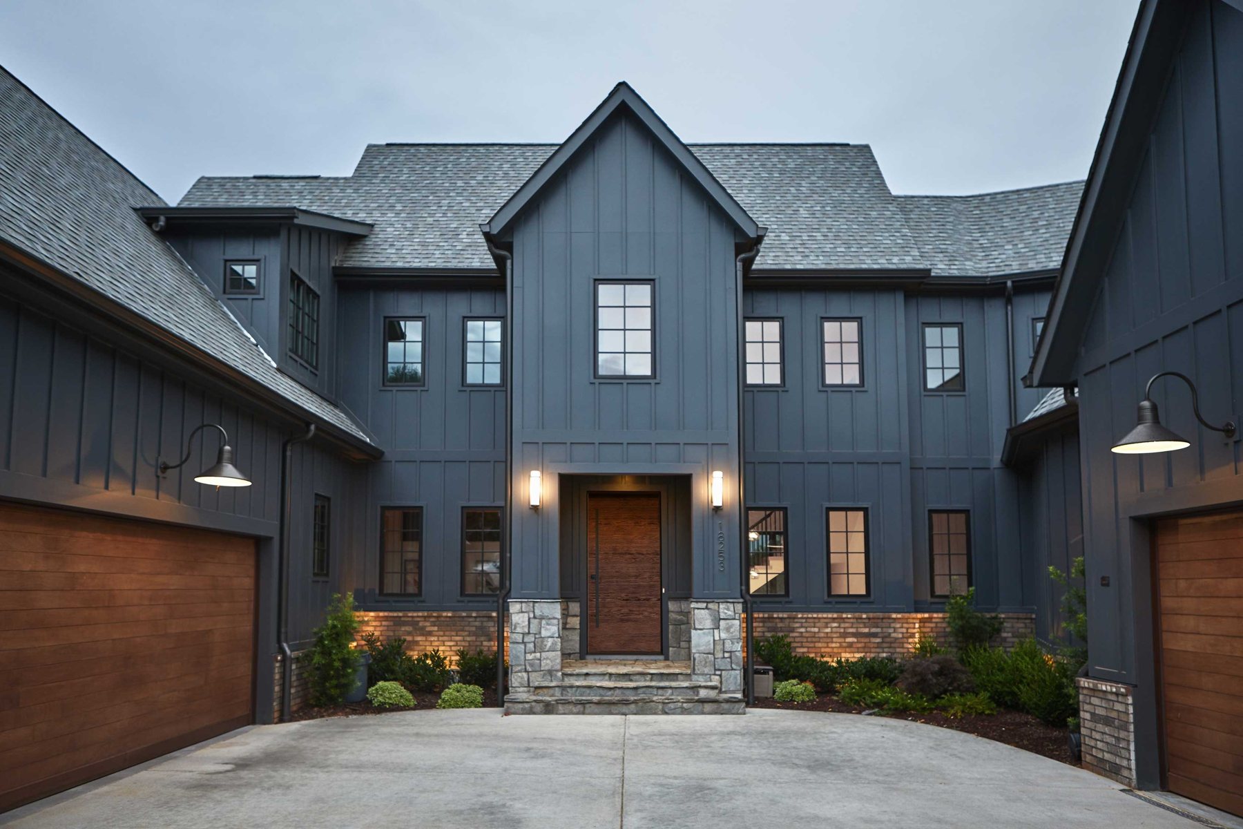 Modern farmhouse exterior with large black-framed windows and lit entry, the kind of home we supply windows and doors for
